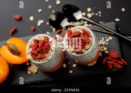 Dietetici di chia budino di sementi con bacche di goji, fracassato di albicocca fresca e fiocchi di avena su nero ardesia bordo. Sfondo nero con copia spazio. Dieta Fitness Foto Stock