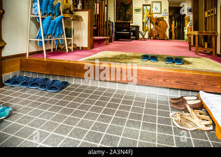 File di pantofole colorate allineano l’area d’ingresso con pavimento in tatami del Ryokan Izu Makiba a Nishiizu-Cho, prefettura di Shizuoka, Giappone. È consuetudine togliersi le scarpe prima di entrare in una casa giapponese. Foto Stock