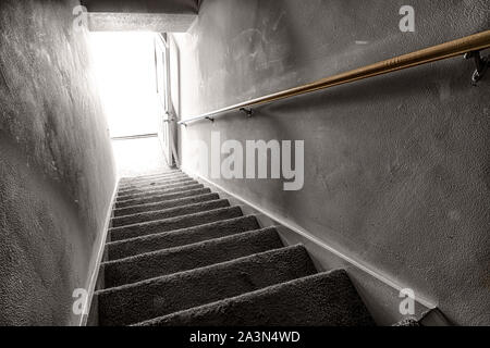 Inquadratura orizzontale guardando giù per una scalinata verso la luce proveniente da una porta aperta sul fondo. Foto Stock