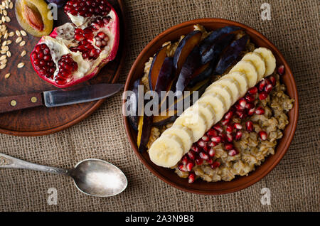 Immagine ravvicinata di una ciotola con il porridge di avena, banana, i semi di melograno e prugna su un letto di sacco dello sfondo. Il sovraccarico laici piatta Foto Stock