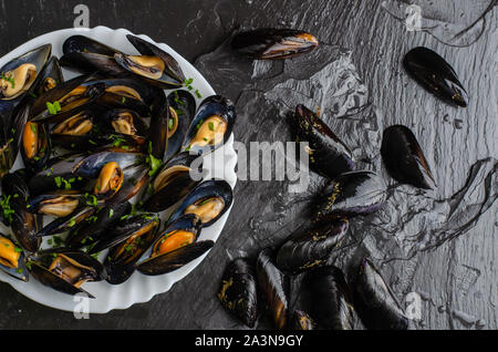 Crudo fresco e cozze cotte su lastre di ardesia nera sullo sfondo di pietra. Concetto di frutti di mare. Vista superiore, laici piatta Foto Stock