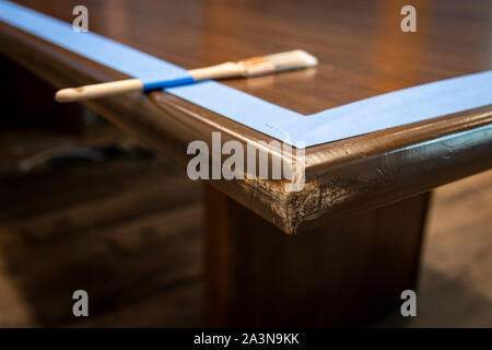 Pennello sul bordo del tavolo da conferenza; preparato con nastro da pittore per uno strato fresco di vernice smalto Foto Stock