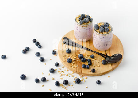 Dieta di deliziosi dessert. Yogurt fatto in casa con mirtilli e avena sulla tavola di legno e sfondo bianco. Spazio di copia Foto Stock