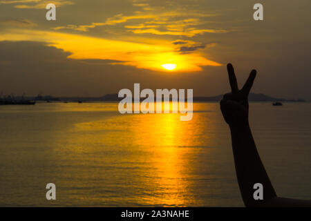 Silhouette di due dita della donna la mano o la vittoria davanti al sun durante l'orario del tramonto. Concetto di combattimento Foto Stock