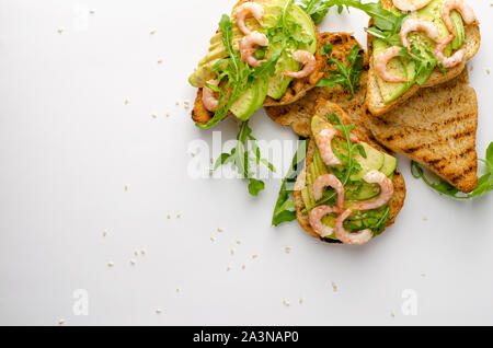 Dieta sana antipasto. Avocado toast con rucola e gamberetti su piastra bianca. Overhead shot, spazio di copia Foto Stock