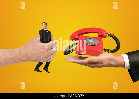Grande maschio passando la mano minuscola imprenditore per un altro canto con retro telefono rosso su sfondo giallo Foto Stock