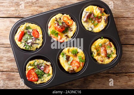 Uovo muffin frittata con pancetta, pomodori, spinaci e funghi close-up in una teglia sul tavolo. Parte superiore orizzontale vista da sopra Foto Stock