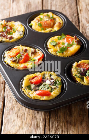 Uovo muffin frittata con pancetta, pomodori, spinaci e funghi close-up in una teglia sul piano verticale. Foto Stock