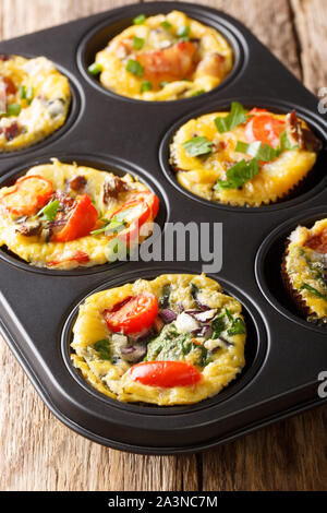 Gustosi piatti caldi muffin di uova con bacon, pomodori, spinaci e funghi close-up in una teglia sul piano verticale. Foto Stock
