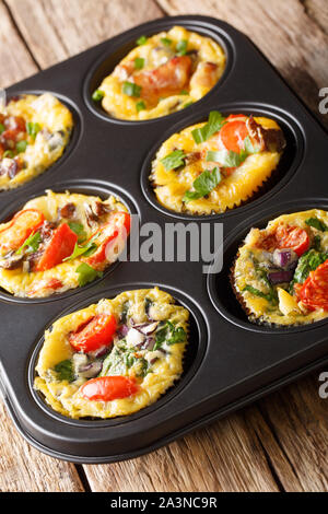 Colazione muffin uovo con pancetta affumicata, pomodori, spinaci e funghi close-up in una teglia sul piano verticale. Foto Stock
