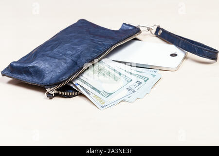 Aprire blu braccialetto in pelle borsetta borsa con smartphone e dollari USA su marrone pallido tabella Foto Stock