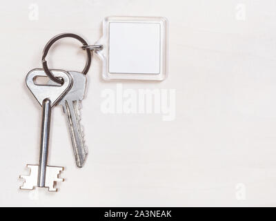 Due tasti della porta sul portachiavi con vuoto portachiavi bianco su marrone pallido tabella Foto Stock