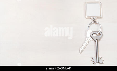 Due tasti della porta sul portachiavi con carta bianca portachiavi su panoramica marrone pallido board Foto Stock