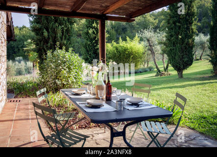 Chianti, Toscana, Italia, settembre 2019. Tavolo per il pranzo sotto un patio di fronte ad un giardino Foto Stock