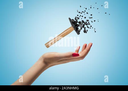 Femmina di mano che tiene un martello piccolo frantumarsi in pezzi su sfondo blu Foto Stock