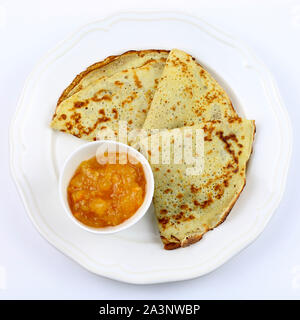 Crepes piegato in quattro sulla piastra bianca e amara marmellata di arance in un bicchiere su sfondo bianco. Vista superiore Foto Stock