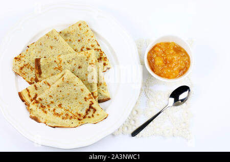 Crepes piegato in quattro sulla piastra bianca e amara marmellata di arance in un bicchiere su sfondo bianco. Vista superiore Foto Stock