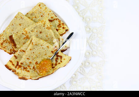 Crepes piegato in quattro sulla piastra bianca e marmellata di arance amare con cucchiaio su sfondo bianco. Vista superiore Foto Stock