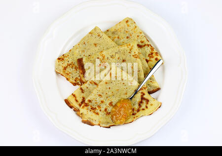 Crepes piegato in quattro sulla piastra bianca e marmellata di arance amare con cucchiaio su sfondo bianco. Vista superiore Foto Stock