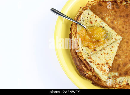 Crepes piegato in quattro sulla piastra di colore giallo e marmellata di arance amare con cucchiaio su sfondo bianco. Vista superiore Foto Stock