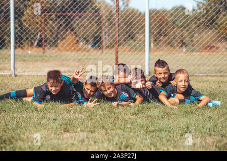 Kids soccer football - bambini giovani giocatori celebrando la vittoria insieme sdraiati sull'erba. Foto Stock