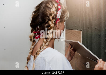 Il giovane bella ragazza fa il lavoro dell'uomo non riparazione e funziona con una piastrella utilizza un livello. Il concetto di costruzione e di riparazione delle donne e del lavoro per donna Foto Stock