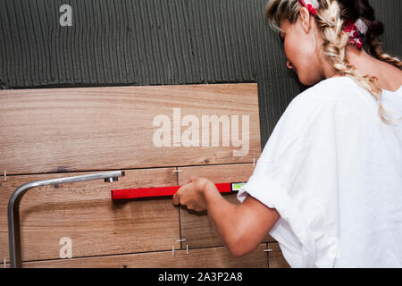 Il giovane bella ragazza fa il lavoro dell'uomo non riparazione e funziona con una piastrella utilizza un livello. Il concetto di costruzione e di riparazione delle donne e del lavoro per donna Foto Stock