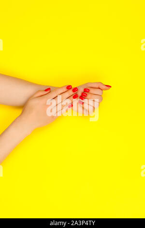 Alla moda ed elegante femmina rosso manicure. Giovane e bella donna di mani su sfondo giallo. Foto Stock