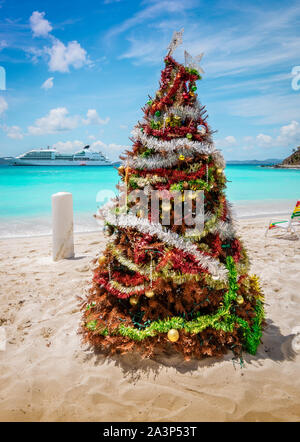 Albero di Natale decorato sulla sabbia bianca della spiaggia caraibica, Jost Van Dyke, Isole Vergini Britanniche. La nave di crociera in background. Foto Stock