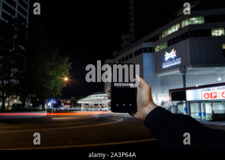 Un telefono cellulare con le parole rideshare sullo schermo sovrapposto ad una vista di una strada di città nel centro cittadino di Vancouver. Foto Stock