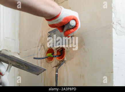 Un lavoratore è in possesso di cazzuole con un gesso. Essa è la copertura di una elettrica tubi corrugati nella parete. Foto Stock