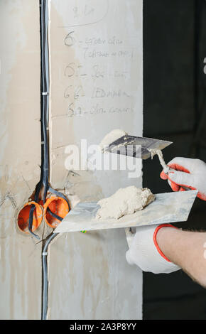 Un lavoratore è in possesso di cazzuole con un gesso. È il rivestimento di cavi elettrici in parete. Foto Stock