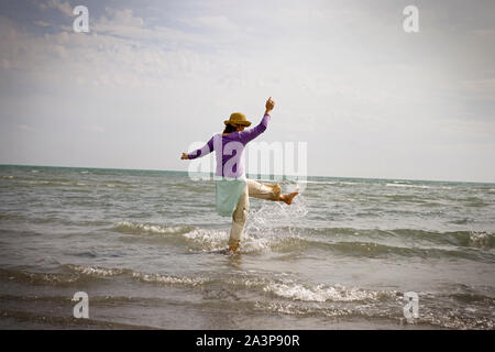 Metà donna adulta di calci e spruzzi in mare. Foto Stock