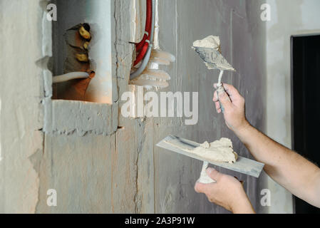 Un lavoratore è in possesso di cazzuole con un gesso. Essa è la copertura di una elettrica tubi corrugati nella parete. Foto Stock