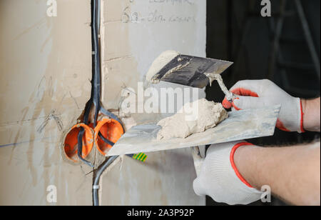 Un lavoratore è in possesso di cazzuole con un gesso. È il rivestimento di cavi elettrici in parete. Foto Stock