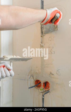 Un lavoratore è in possesso di cazzuole con un gesso. Essa è la copertura di una elettrica tubi corrugati nella parete. Foto Stock