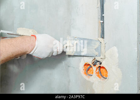 Un lavoratore è in possesso di cazzuole con un gesso. Essa è la copertura di una elettrica tubi corrugati nella parete. Foto Stock