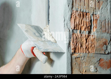 Un lavoratore è in possesso di cazzuole con un gesso. Essa è la copertura di una elettrica tubi corrugati nella parete. Foto Stock