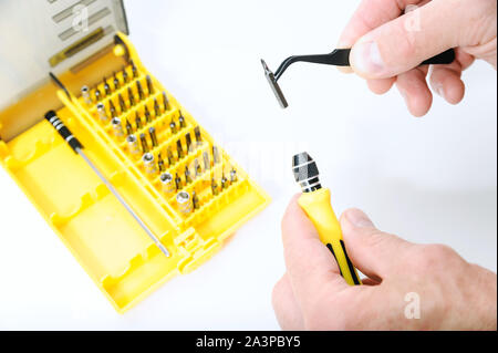 Un uomo è utilizzando pinzette per inserire un bit in un cacciavite. Accanto vi è un insieme di bit. Foto Stock