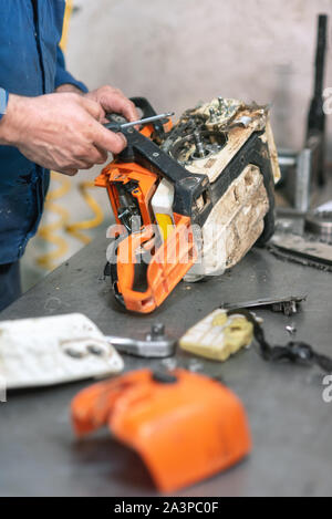 Riparazione meccanica di una sega elettrica. Uomo che ripara un chainsaw nel banco di lavoro . Foto Stock