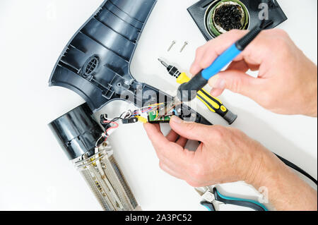 Asciugacapelli in una condizione disassemblata su uno sfondo bianco. L'uomo è la riparazione di esso. Foto Stock