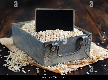 Bianco crudo grano di sorgo in una scatola di metallo con una piccola lavagna Foto Stock