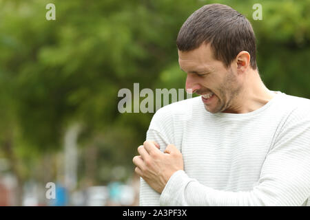 Uomo che soffre di prurito cratching braccio in piedi in un parco Foto Stock