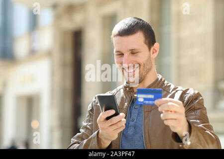 Adulto felice moda uomo pagando con carta di credito e il telefono cellulare in piedi in strada Foto Stock