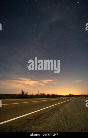 Strada asfaltata scompare all'orizzonte di notte sotto un profondo, blu cielo stellato. Foto Stock