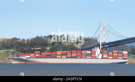 San Francisco, CA - 18 Febbraio 2019: Nave da carico PONTE DI HANNOVER con partenza dal Porto di Oakland, il Ponte della Baia e l'Isola del Tesoro in background. Foto Stock