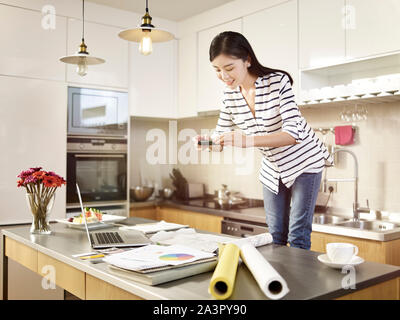 Giovane donna asiatica professional designer che lavora a casa di scattare una foto del suo design utilizzando il telefono cellulare. Foto Stock