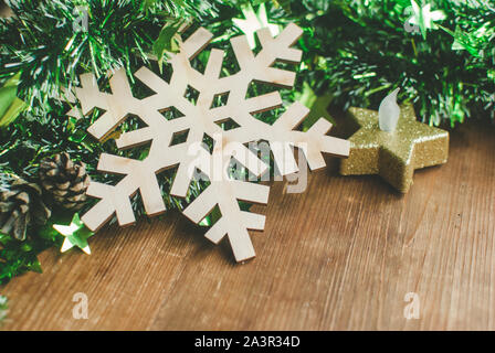 Sfondo di natale con composizione decorativa di tinsel verde, legno simbolo del fiocco di neve, candela e cono di pino sulla tavola di legno. Foto Stock