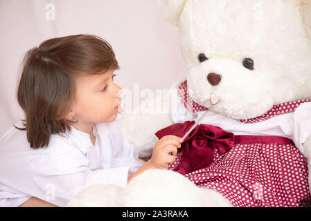 Bambina vestito come un dentista esaminando un orso di peluche Foto Stock