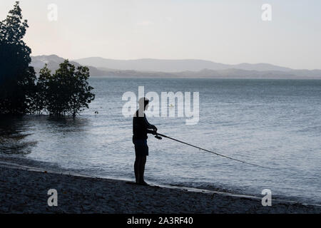 Silhouette di un pescatore di pesca sulla spiaggia al tramonto, Elim Spiaggia, Lontano Nord Queensland, FNQ, QLD, Australia Foto Stock